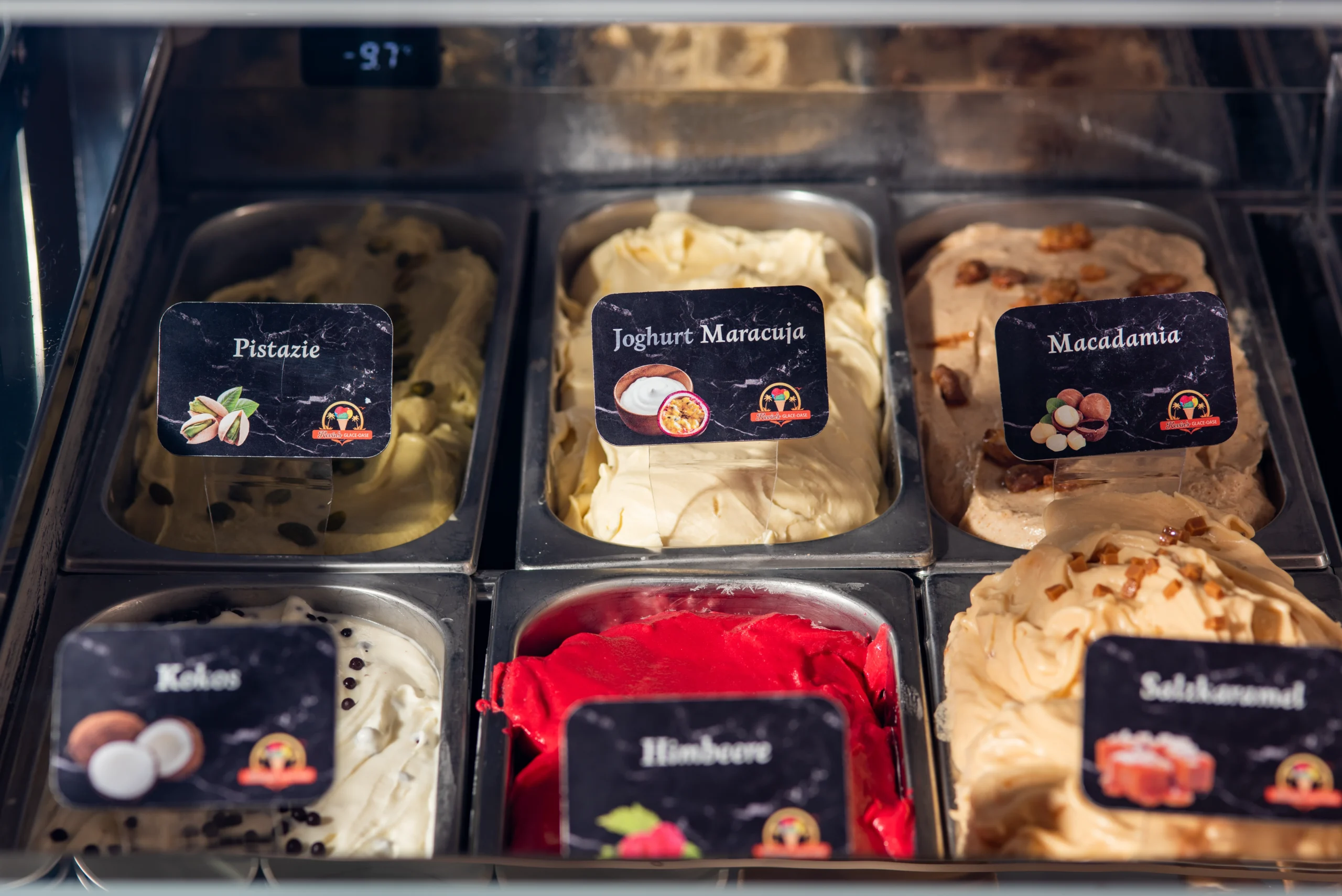 Eistheke mit verschiedenen Sorten wie Pistazie Joghurt Maracuja Macadamia Himbeere und Kokos in Edelstahlbehaeltern.